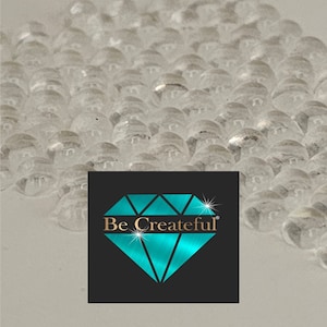May include: A close-up image of a sheet of clear, round, plastic gems. The gems are arranged in rows and are slightly overlapping. The gems are all the same size and shape. The background is a light gray color. The image includes the text "Be Createful" in a diamond shape.