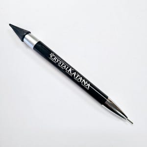 May include: A black pencil with a silver tip and a black pointed tip on the other end. The pencil has the text "CRYSTAL KATANA" printed on it.