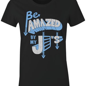 Puede incluir: Camiseta negra para mujer con un diseño gráfico azul y blanco que dice "Be Amazed By My J's".