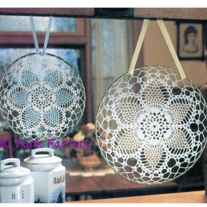 May include: Two white crocheted doilies are hanging from the ceiling. The doilies are circular and have a delicate floral design. They are hanging from white and yellow ribbons.