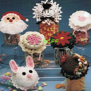 Könnte beinhalten: Häkel-Gläserdeckel in verschiedenen Urlaubsthemen, darunter Weihnachtsmann, Spinne, Blume, Hase und Truthahn. Die Gläser sind mit bunten Süßigkeiten gefüllt.
