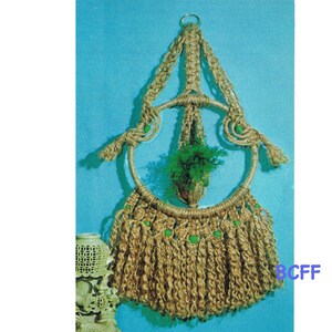 May include: A macrame plant hanger with a circular base and green beads. The hanger is made of natural fibre rope and has a fringe at the bottom.