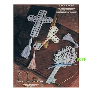 May include: A set of three white crocheted bookmarks. One bookmark is a cross, another is a key, and the third is a flower. The bookmarks are on a brown surface with the text "KEY TO KNOWLEDGE" and "LACE CROSS" visible.