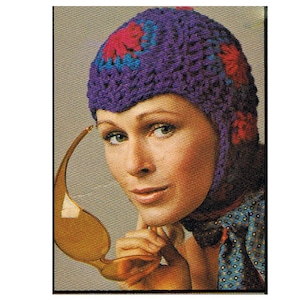 May include: A purple crocheted hat with pink and blue flower accents. The hat has ear flaps and a pointed crown.