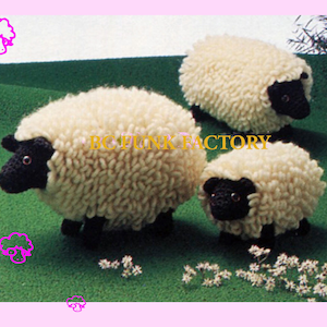 Puede incluir: Tres ovejas de crochet blanco con caras negras. Las ovejas están sentadas sobre una superficie verde cubierta de hierba.