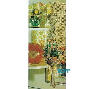May include: A macrame plant hanger with a brown pot and green plant. The hanger is made of natural rope and has wooden beads in yellow, green, and brown. The hanger is hanging in front of a wall with a floral wallpaper pattern.