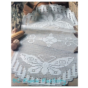 Puede incluir: Un camino de mesa de crochet blanco con un delicado patrón floral. El camino de mesa está hecho con un hilo fino y tiene un borde festoneado.