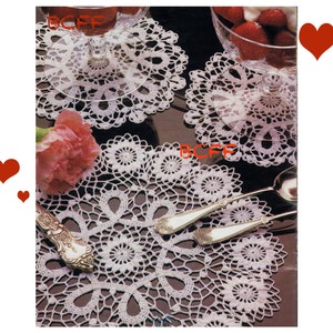 May include: Three white crocheted doilies with intricate designs. The doilies are arranged on a dark surface with a glass bowl of strawberries and whipped cream in the background.