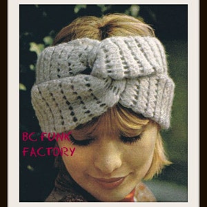 Può includere: Primo piano di una donna che indossa una fascia per capelli in crochet grigia con un design annodato. La fascia è indossata sopra i capelli e copre la fronte. La donna guarda in basso e sorride. Il testo "BC FUNK FACTORY" è visibile nell'angolo in basso a sinistra dell'immagine.