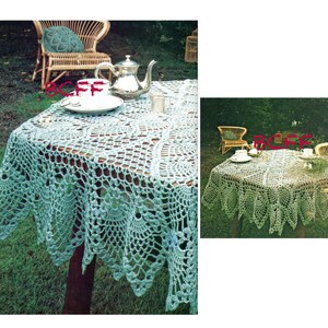 May include: A crocheted tablecloth with a delicate lace pattern in a light blue colour. The tablecloth is laid out on a wooden table with a teapot and cups on top. The table is set in a garden setting with green grass and trees in the background.