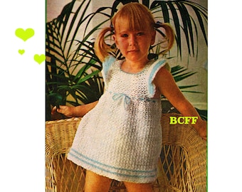 May include: A white crochet dress with blue trim and a bow at the waist. The dress is being worn by a young girl with blonde hair and pigtails. The girl is sitting in a wicker chair in front of a potted plant.