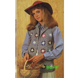 Puede incluir: Un chaleco de ganchillo con un patrón floral colorido. El chaleco tiene un cuello chal y se lleva sobre una camisa azul claro. La persona lleva un sombrero rojo y sostiene una cesta de flores.