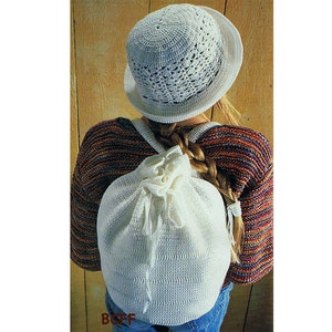 May include: A white crocheted backpack with a drawstring closure. The backpack is being worn by a person with a white crocheted hat and a colourful striped jumper.