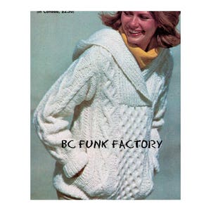 Op de afbeelding: Een witte gebreide cardigan met een grote kraag en een capuchon. De cardigan heeft een kabelbreipatroon en een zak aan de voorkant. De tekst "BC FUNK FACTORY" is gedrukt op de voorkant van de cardigan.