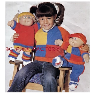 Könnte beinhalten: Ein Mädchen hält zwei Cabbage Patch Kids Puppen. Die Puppen tragen gestrickte Outfits in Rot, Blau und Gelb. Das Mädchen trägt einen blau-gelb-roten Pullover.