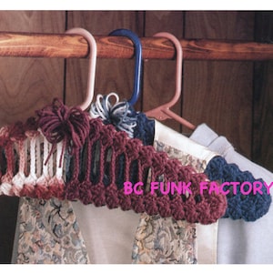 May include: Three crocheted hangers in pink, burgundy, and blue hanging on a wooden closet rod. The hangers are made with a simple stitch pattern and have a decorative bow at the top. The text "BC FUNK FACTORY" is visible in the image.