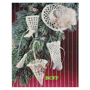Op de afbeelding: Witte gehaakte kerstversieringen in de vorm van een laars, een hoed, een paraplu en een kous. De versieringen hangen aan een groene kerstboom.