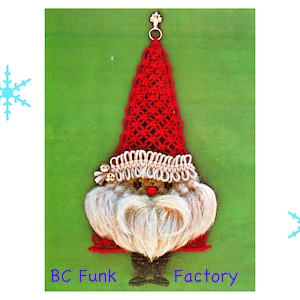 Op de afbeelding: Een rood en wit gehaakte gnoom ornament met een witte baard en een bel op de hoed. De gnoom hangt aan een groene achtergrond. BC Funk Factory.