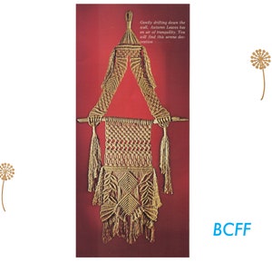 K&ouml;nnte beinhalten: Ein Wandbehang aus Makramee mit dreieckiger Form und Quasten. Der Behang ist aus Naturfaserseil gefertigt und hat oben einen Holzstab. Der Text "Gently drifting down the wall, Autumn Leaves has an air of tranquility. You will find this serene decoration" ist auf dem Bild gedruckt.