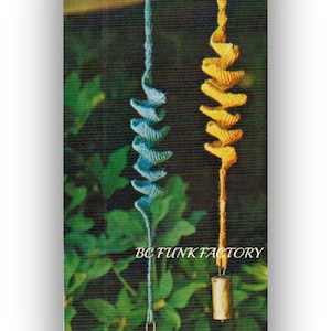 Op de afbeelding: Twee gebreide windgong met bellen die aan een veranda hangen. De windgong links is blauw en de windgong rechts is geel. De tekst "BC FUNK FACTORY" is zichtbaar in de afbeelding.