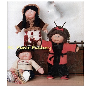 Könnte beinhalten: Drei Cabbage Patch Kids Puppen, die handgemachte gestrickte Outfits tragen. Die Puppe links trägt einen blauen Hut, einen cremefarbenen Pullover mit rotem und weißem Muster und eine blaue Hose. Die Puppe in der Mitte trägt eine rot-schwarze Robe mit einem schwarzen Gürtel. Die Puppe rechts trägt einen braunen Pullover mit cremefarbener Einfassung, eine weiße Hose mit braunem und weißem Kuhmuster und einen braunen Hut mit cremefarbener Einfassung.