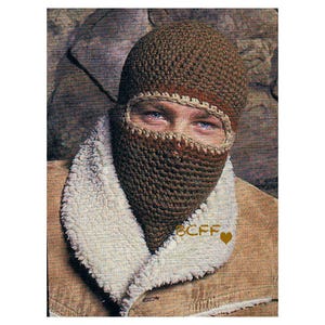 May include: A brown crocheted balaclava with a brown and red trim. The balaclava is worn by a person with a brown jacket and a white fur collar.