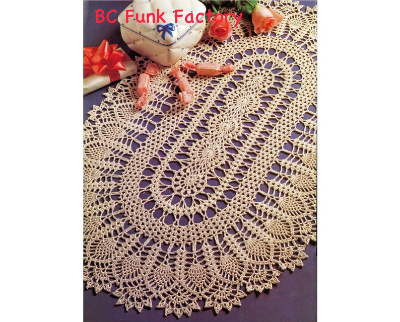 May include: A beige crocheted oval table runner with a delicate lace pattern. The runner is on a purple background.