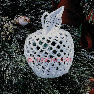 May include: White crocheted apple ornament with a delicate openwork design. The ornament is hanging on a green evergreen tree branch.