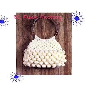 Op de afbeelding: Een witte gehaakte handtas met een bruine houten handvat. De tas heeft een textuur, een bolvormig ontwerp.