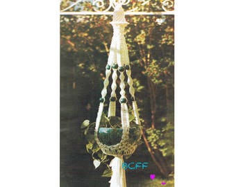 May include: White macrame plant hanger with green beads and a green ceramic pot with a plant inside.