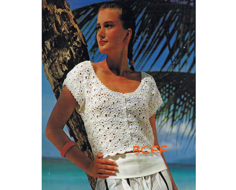 Puede incluir: Un top blanco de crochet con cuello redondo y mangas cortas. El top tiene un cierre de bot&oacute;n en la parte delantera y un patr&oacute;n de crochet.