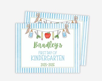 May include: Two rectangular cards with a blue and white striped border. The cards feature a banner of school supplies and the text "Bradley's First Day of Kindergarten 2025-2026" in green and blue.
