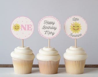 May include: Three cupcakes with pink and white polka dot, pink and white gingham, and white cupcake toppers. The toppers feature a smiling sun with a pink bow and the text "One", "Happy Birthday Mary", and "Little Sunshine".