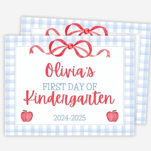 May include: Two stacked, rectangular signs with a light blue gingham border. The top of each sign features a red bow. The text reads "Olivia's First Day of Kindergarten 2024-2025" in red and blue. Red apple illustrations are on each side.