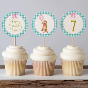 May include: Three cupcakes with decorative toppers. One topper says "Happy Birthday Charlee!" with a pink bow. Another features a dog with a pink balloon. The third has the number 7. All toppers have a teal and white gingham border.