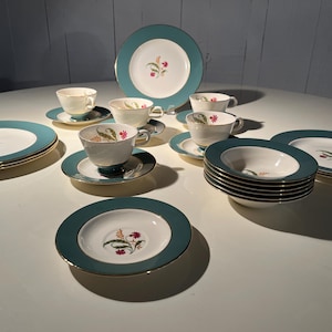 May include: A vintage teal and white china set with gold trim. The set includes plates, saucers, bowls, and teacups, each adorned with a floral design. The plates measure approximately 25 cm in diameter.