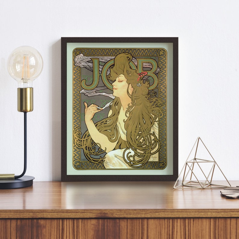 Puede incluir: Un cartel vintage de estilo art nouveau con una mujer de cabello largo y fluido, sosteniendo una pluma estilogr&aacute;fica. El cartel est&aacute; enmarcado en un marco marr&oacute;n oscuro y tiene un fondo verde y dorado con la palabra "JOB" en la esquina superior izquierda.