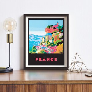 May include: A framed poster with a colorful illustration of a village in France. The village is built on a cliff with a church at the top. The poster has the word "FRANCE" in pink letters at the bottom.