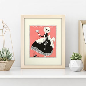 Może przedstawiać: Ilustracja w ramie przedstawiająca kota ubranego w str&oacute;j pokoj&oacute;wki, trzymającego pi&oacute;ropusz. Kot ma na sobie czarną sukienkę z białym fartuchem i białym czepkiem. Tekst "The Coconut Cat" jest nadrukowany nad kotem. Ilustracja jest na r&oacute;żowym tle.
