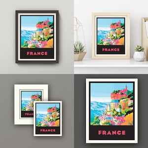 May include: A colorful illustration of a French village with the word "FRANCE" printed in pink letters. The village is situated on a cliff overlooking a valley. The illustration is framed in black.