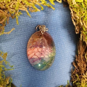 May include: A colorful, iridescent, resin pendant with a silver bail. The pendant is oval shaped and has a swirling pattern of pink, blue, green, and yellow.