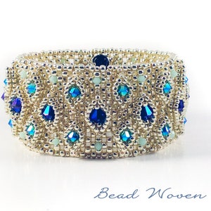 May include: A silver beaded bracelet with blue and green crystals. The bracelet is woven in a geometric pattern.