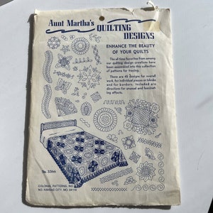 May include: Vintage Aunt Martha's Quilting Designs pattern packet. The packet features various quilting designs, including floral and geometric patterns, and a bed quilt design. The text reads "Enhance the Beauty of Your Quilts."