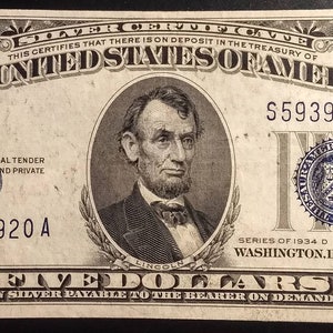 May include: A vintage five dollar silver certificate from 1934. The bill features a portrait of Abraham Lincoln and the text "The United States of America". The serial number is S59394920 A.