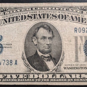 May include: A vintage five dollar silver certificate featuring a portrait of Abraham Lincoln. The certificate is dated 1934 and has the serial number R09254738 A.