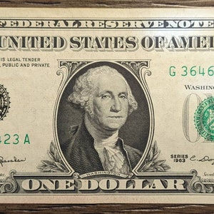 May include: A one dollar bill featuring a portrait of George Washington. The bill is green and has the words "THE UNITED STATES OF AMERICA" printed on it. The serial number is G 36462423 A.