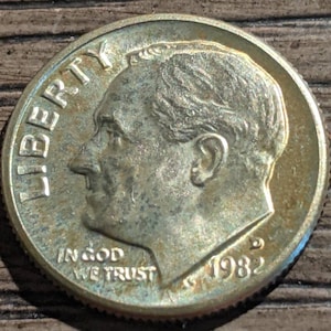 Puede incluir: Una moneda de diez centavos estadounidense de plata con las palabras "LIBERTY" e "IN GOD WE TRUST" inscritas en el anverso. El año "1982" es visible en el lado derecho de la moneda.