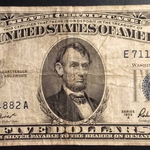 May include: A five dollar silver certificate from the United States of America, featuring a portrait of Abraham Lincoln. The serial number is E 71184882 A. The certificate is dated 1953 and signed by the Secretary of the Treasury, Robert Anderson.
