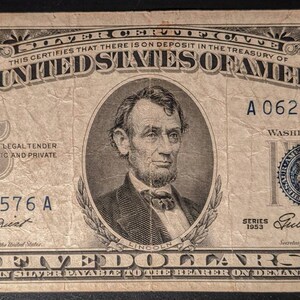 May include: A vintage five dollar silver certificate featuring a portrait of Abraham Lincoln. The serial number is A 06247576 A. The certificate is dated 1953 and signed by the Secretary of the Treasury.