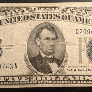 May include: A vintage five dollar bill featuring a portrait of Abraham Lincoln. The bill is dated 1934 and has the serial number Q20949743A. The bill is in good condition and has a blue seal.